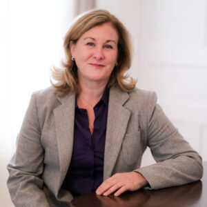 Jennifer McGill, President of AMBICO, seated at a table with a wooden finish, looking directly at the camera for a corporate headshot. 